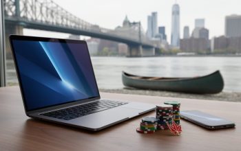 Laptop and smartphone next to poker chips and a red maple leaf pin on a wooden table, with a blurred river, steel bridge, distant skyline, and a beached canoe in the background.