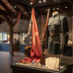 Interior view of the Kentucky Military History Museum with displayed battle flags, a vintage rifle, medals, and personal letters in a museum case.